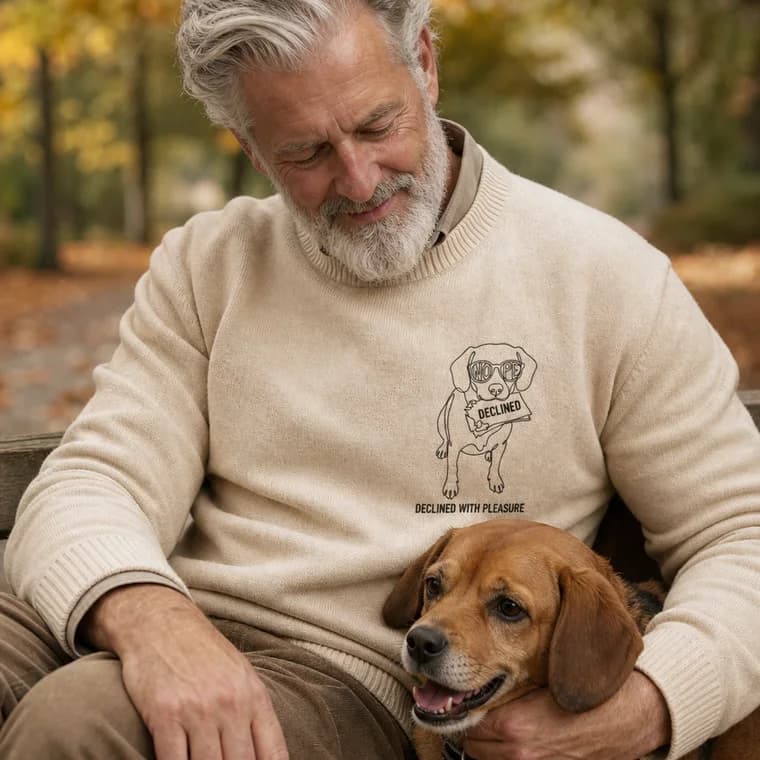 A man with his beagle, wearing a sweater embroidered with the DECLINED WITH PLEASURE design