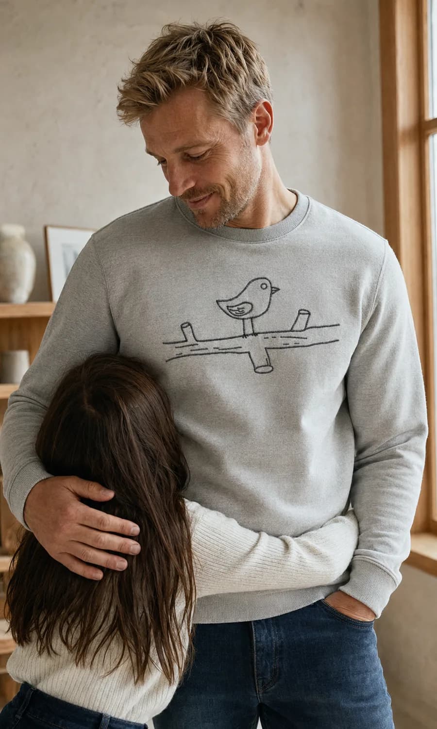 A father hugging his daughter, wearing a sweatshirt embroidered with her bird drawing