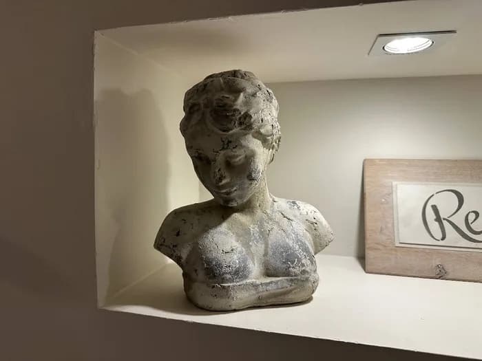 A weathered plaster bust standing in a lit wall niche
