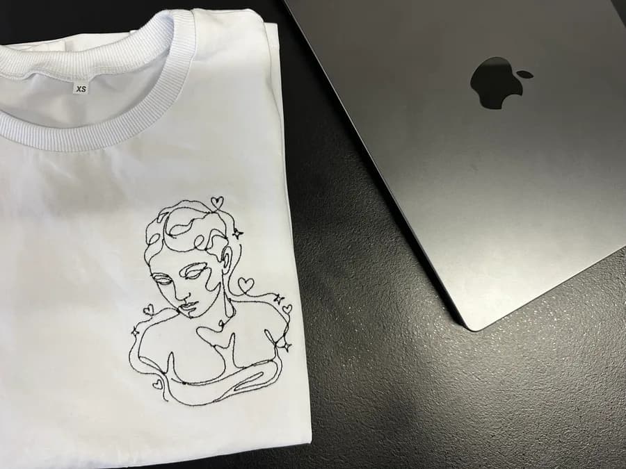 A white t-shirt embroidered with a one-line drawing of a classical bust